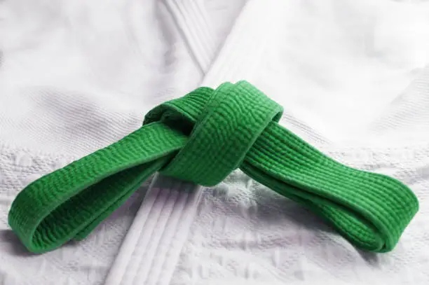 Green martial art belt tied in a knot on white gi in backgroundBrown martial art belt tied in a knot on blue background