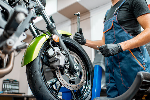 Mechanic in overalls repairing sports motorcycle at the workshop indoors