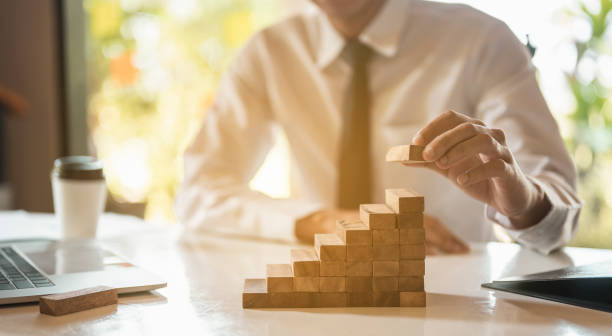 Businessman hand pulling out or placing wood block on the  tower and semi-pyramid in modern office. Plan and strategy in business. stock photo