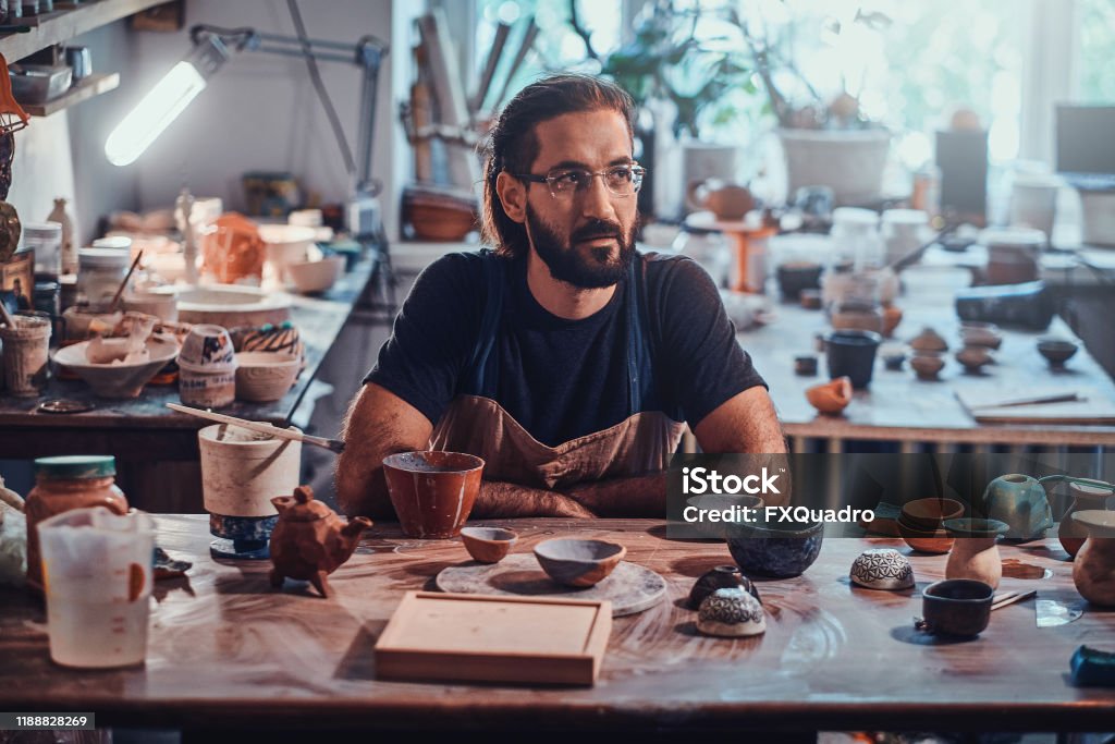 Happy man in glasses is sitting at his owh workshop and his projects are around him. Charismatic happy man in glasses is sitting at his owh workshop and his projects are around him. Adult Stock Photo
