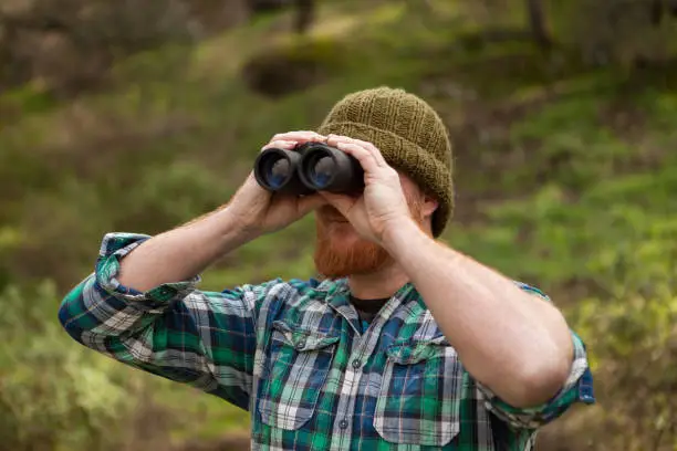 Red haired man looking throw a binocular in the field
