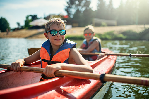 Two boys enjoying kayaking on lake on sunny summer day.\nNikon D810