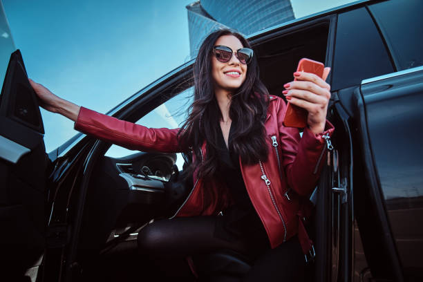 Beautiful smiling women is posing in her new car while chatting on mobile phone