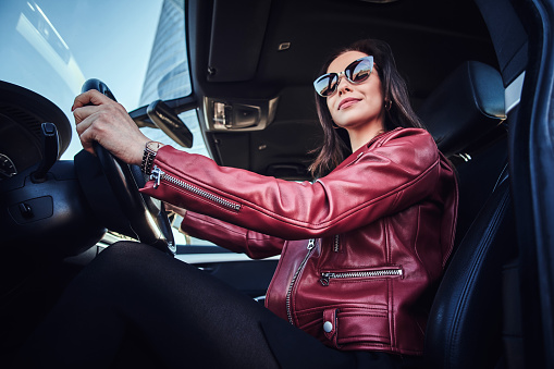 Attractive young woman in red jacket and sunglasses in driving her car.