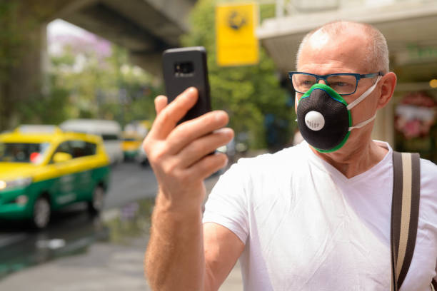 istock Senior man using face mask to protect from pollution smog in city while holding mobile phone 1188844253