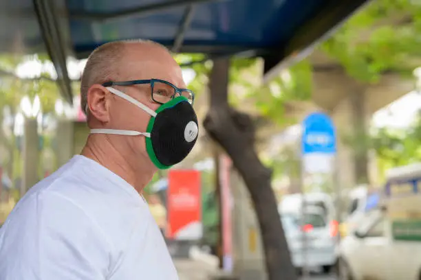 Photo of Senior man using face mask to protect from pollution smog in city