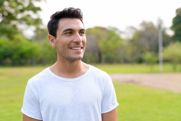 Face of happy young handsome Hispanic man thinking at the park Portrait of young handsome Hispanic man in the park outdoors 30 34 years stock pictures, royalty-free photos & images