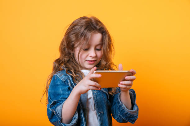 istock Cute child using a smartphone and smiling on yellow background 1188851951