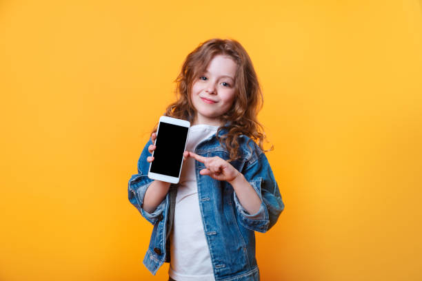 Cute curly girl showing a finger on the phone on yellow background stock photo