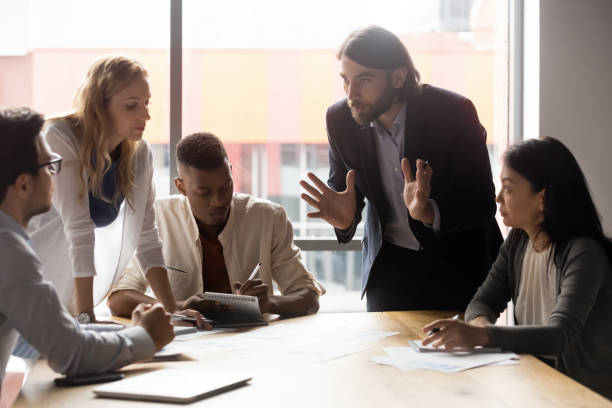 istock Serious young businessman leaning over table, explaining ideas to teammates. 1188856992