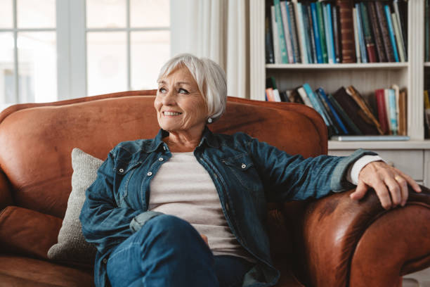 lächelnde seniorin sitzt zu hause auf ihrem sofa - gemütlich stock-fotos und bilder