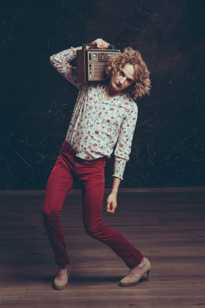 un jeune androgyne dans une chemise avec des fleurs écoute la radio sur une radio vintage. de larges promenades dans le squat. - radio show industry old old fashioned photos et images de collection