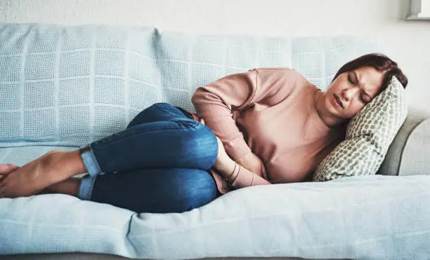 Cropped shot of an attractive young woman lying on her sofa alone and suffering from period cramps at home