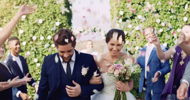 Cropped shot of an affectionate young newlywed couple leaving their wedding venue with their guests throwing confetti in the background