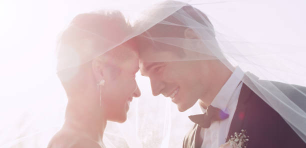 Happy bride looking away while father kissing her on cheek with people in background at outdoor wedding. Horizontal shot.