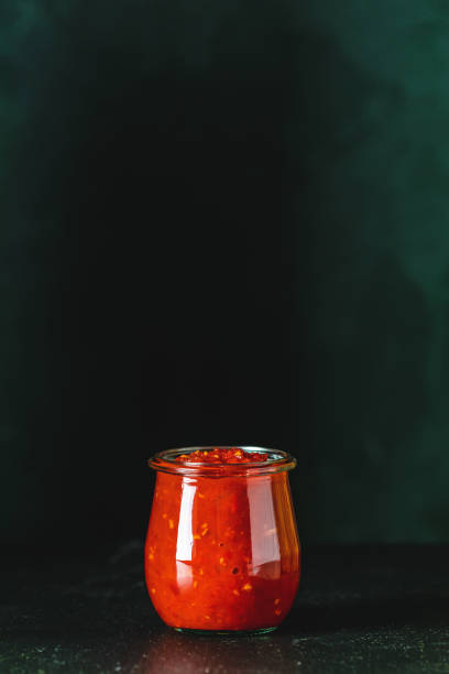 chutney di salsa di pomodoro caldo naturale fai-da-te fatta in casa con peperoncino o adjika in barattolo di vetro in piedi su tavolo di legno, messa a fuoco selettiva - chutney jar tomato preserved foto e immagini stock