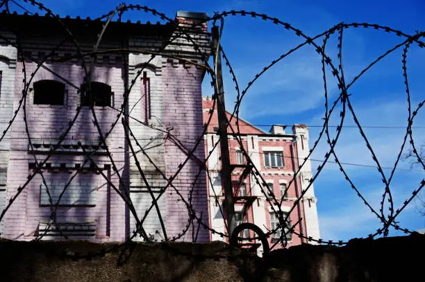 Photo of Close-up of tangled coil of barbed wire on top under blue skies and blurred city street and pink house in the background