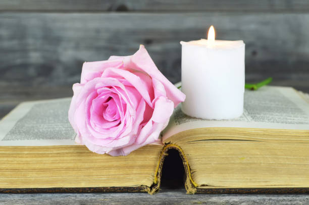 istock Burning white candle and pink rose on open book 1188883196