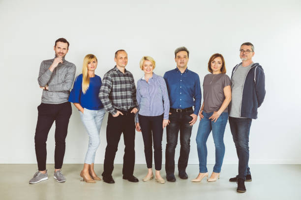 Full length of females and males against white wall. Portrait of confident people standing together. They are wearing casuals.
