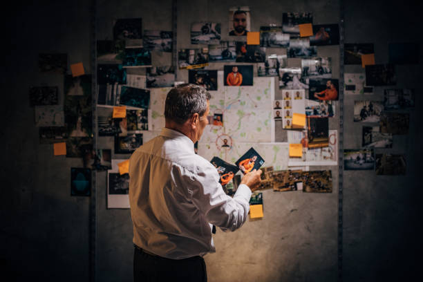 An old detective is looking at photos of suspects in his office An old detective is looking at photos of suspects in his office suspicion photos stock pictures, royalty-free photos & images