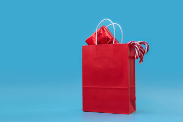 istock Red papers bag with gift boxes and candy sticks on blue background. Christmas and New Year holidays concept. Copy space. Mock-up 1188888070