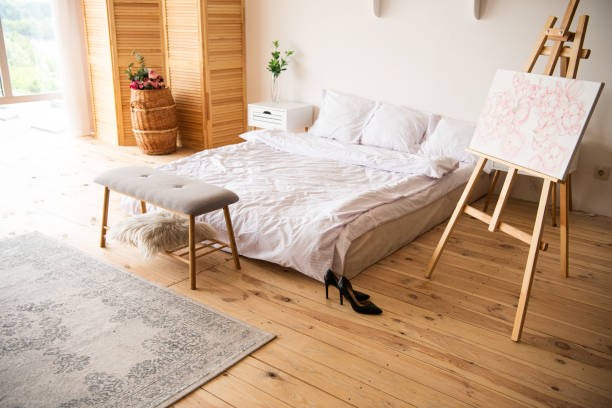 istock bedroom with white blanket and pillows, easel, bedside bench, carpet, room devider and black heels on wooden floor 1188889145