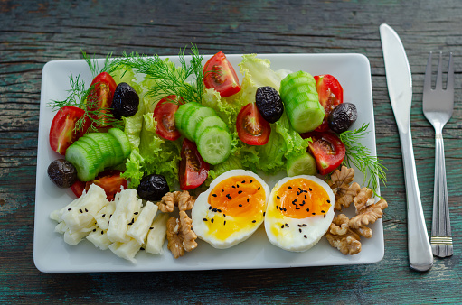 Boiled egg, cheese, dill, lettuce, cucumber, tomatoes and walnuts  for   breakfast on the wooden table.