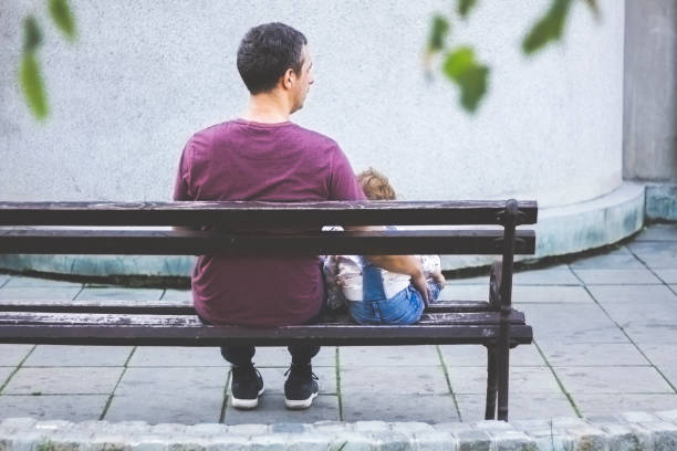Father and his child are sitting on the bench in the park