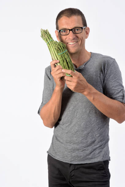 man with food on white background portrait of a man with asparagus on white background eating asparagus stock pictures, royalty-free photos & images