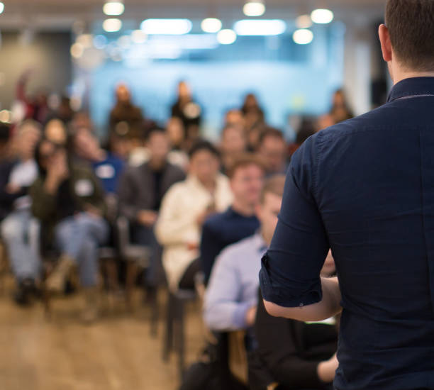 conference photo audience and speaker giving speech. seminar presenter on a panel during forum. corporate manager in sales executive training discussion on stage. investor pitch presentation. - workshop imagens e fotografias de stock