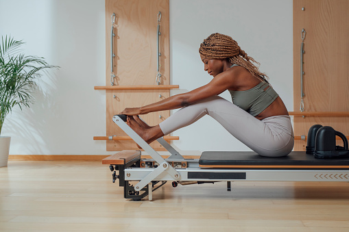 Beautiful African smiling sportswoman doing pilates exercise on reformer.