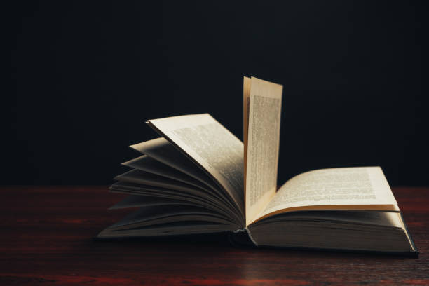 istock One open old book on a red wooden table. Beautiful dark background. 1188900836
