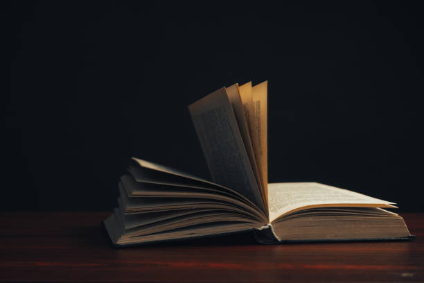 istock One open old book on a red wooden table. Beautiful dark background. 1188900898