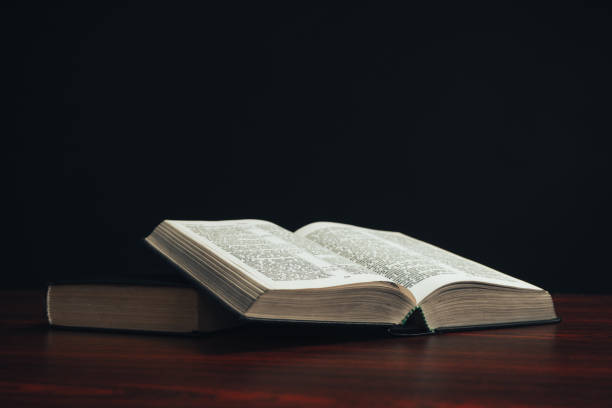 istock Open bible on a  red wooden table. Beautiful black background. 1188900938