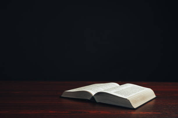 istock Open bible on a  red wooden table. Beautiful black background. 1188900975