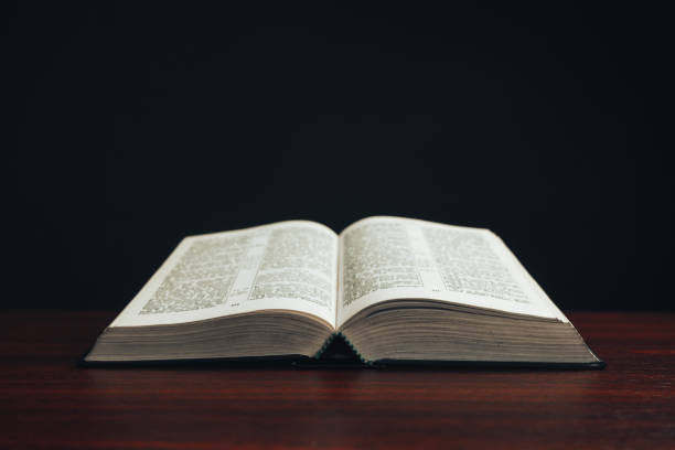 istock Open bible on a  red wooden table. Beautiful black background. 1188901007