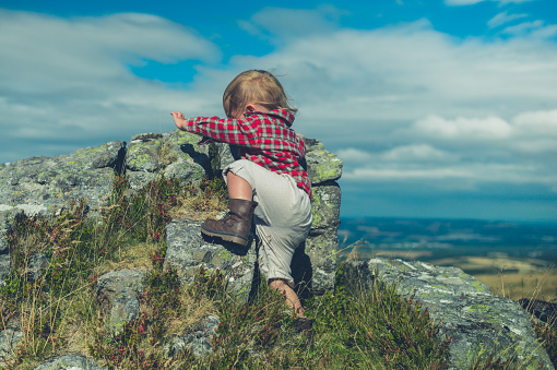 A little toddler is climbing a rock on the moor