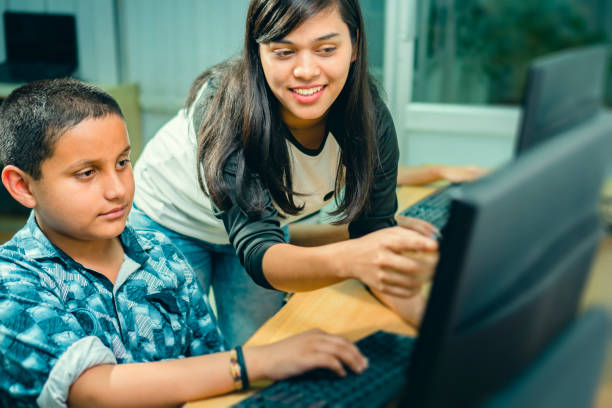 feliz profesora de jóvenes adultos enseña a un estudiante adolescente masculino en una clase de computación. - computer lab child internet development fotografías e imágenes de stock