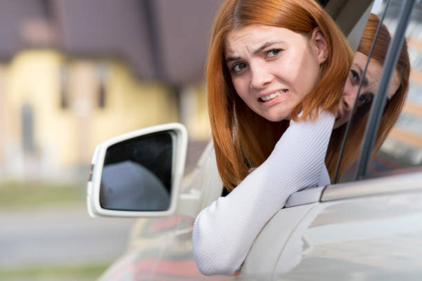 車を後ろ向きに運転している若い女性。彼女は後部車両にフェンダーベンダーのダメージを与えながら、彼女の顔に面白い表情を持つ女の子。 - 逆進 ストックフォトと画像