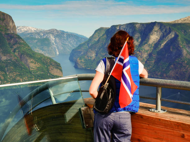 Tourist over Aurlandsfjord with norwegian flag Female tourist with norwegian flag enjoying scenic view over fjord Aurlandsfjord from Stegastein viewing platform. National tourist route Aurlandsfjellet. stegastein viewpoint stock pictures, royalty-free photos & images