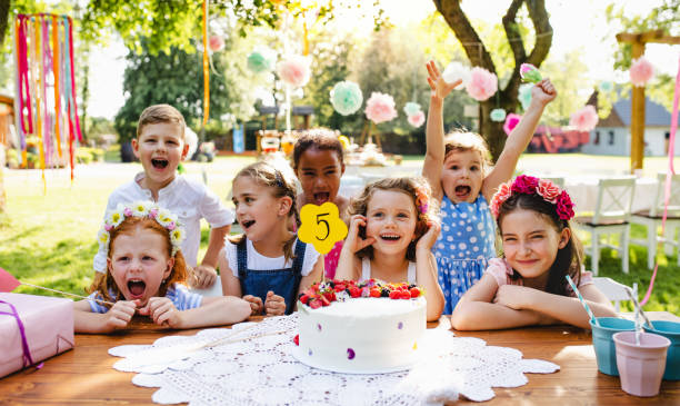 bambini con torta in piedi intorno al tavolo alla festa di compleanno in giardino in estate. - birthday child celebration party foto e immagini stock
