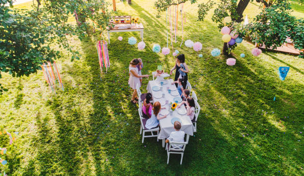 vista de alto ángulo de los niños pequeños sentados en la mesa al aire libre en la fiesta en el jardín. - fiesta en el jardín fotografías e imágenes de stock