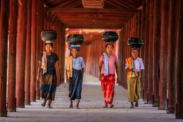Burmese women carrying bowls of rice to the monastery near Bagan, Myanmar
