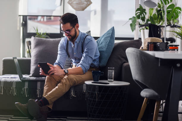 istock Young bearded businessman working on laptop computer while sitting on sofa at his home office 1188911721