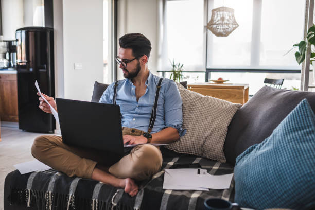 istock Young bearded businessman working on laptop computer while sitting on sofa at his home office 1188911924