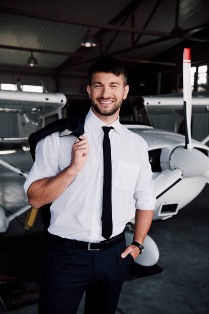 istock smiling pilot in formal wear standing near plane and looking at camera 1188912483