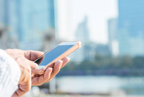 istock close up handsome man using hand typing smartphones and touch screen working search with app devices outdoor in city with sunrise and building background. 5G technology connecting the world. 1188912679