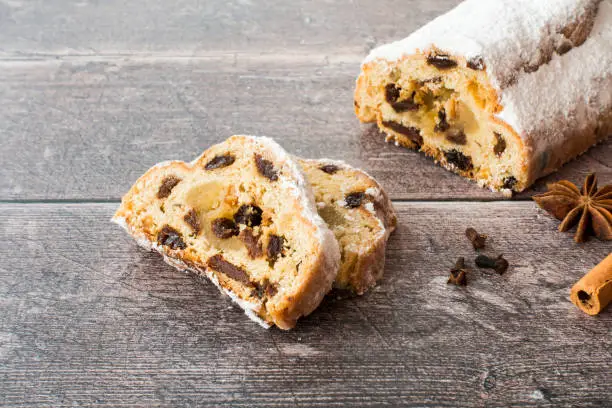 German stollen, Christstollen, with marzipan on dark brown rustic, weathered wood panel background with copy space. Angled view.