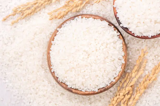 Photo of Raw white polished milled edible rice crop on white background in brown bowl, organic agriculture design concept. Staple food of Asia.