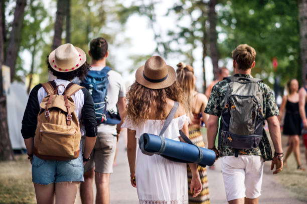 Rear view of group of young friends with backpack walking at summer festival. Rear view of group of young friends with backpack and mat walking at summer festival. clubwear stock pictures, royalty-free photos & images